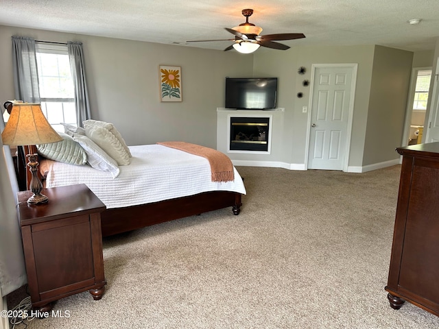 bedroom featuring a glass covered fireplace, baseboards, multiple windows, and light colored carpet