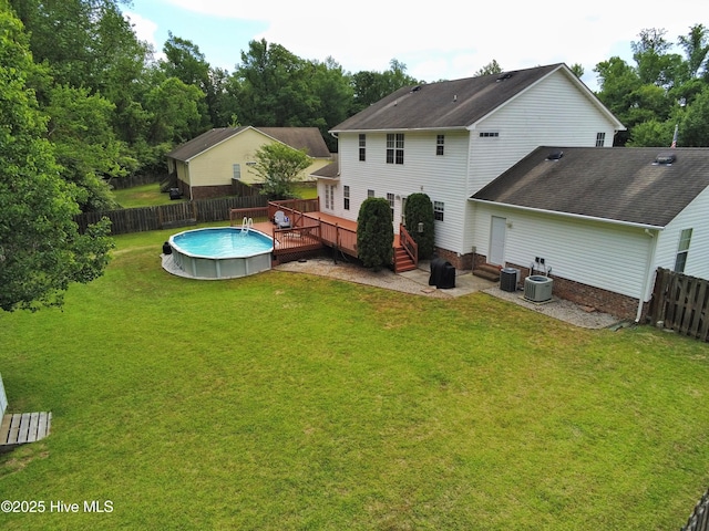 rear view of property featuring a lawn, a deck, central AC, a fenced in pool, and a fenced backyard