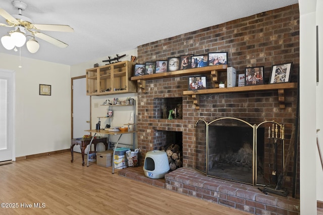 living room with baseboards, wood finished floors, a brick fireplace, and ceiling fan