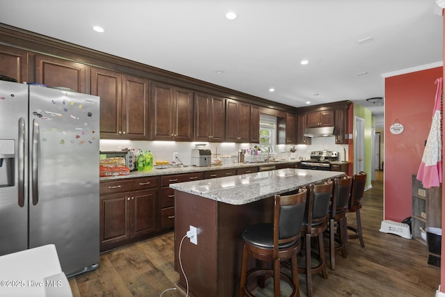kitchen with a center island, crown molding, appliances with stainless steel finishes, dark wood finished floors, and under cabinet range hood