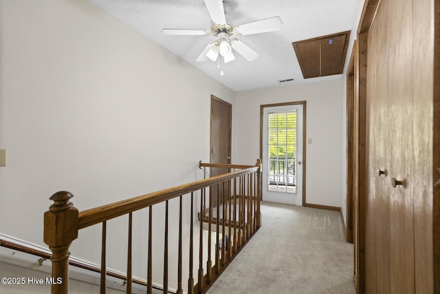 corridor featuring an upstairs landing, a textured ceiling, attic access, carpet flooring, and visible vents
