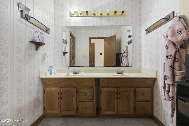 bathroom featuring wallpapered walls, a sink, and double vanity