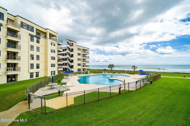 community pool with a yard, a water view, and fence