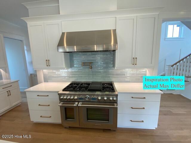 kitchen with exhaust hood, range with two ovens, backsplash, and light wood-type flooring