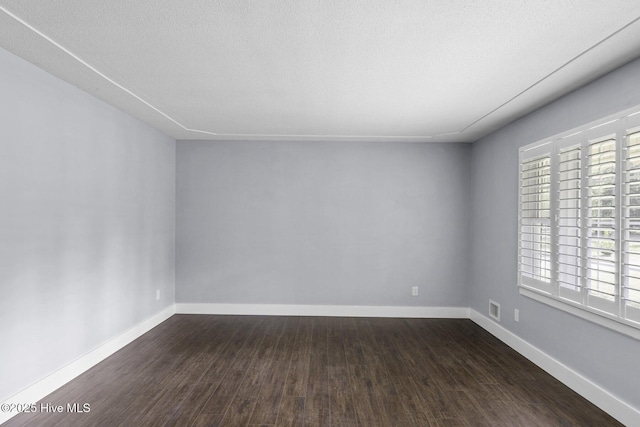 empty room featuring baseboards, visible vents, and dark wood-style floors
