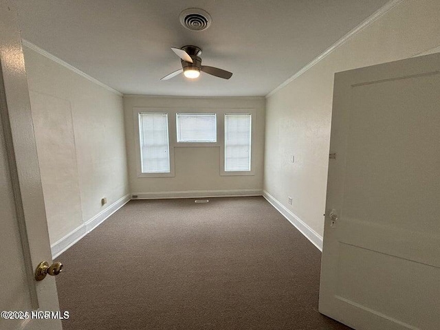 spare room featuring crown molding, dark colored carpet, visible vents, baseboards, and a ceiling fan