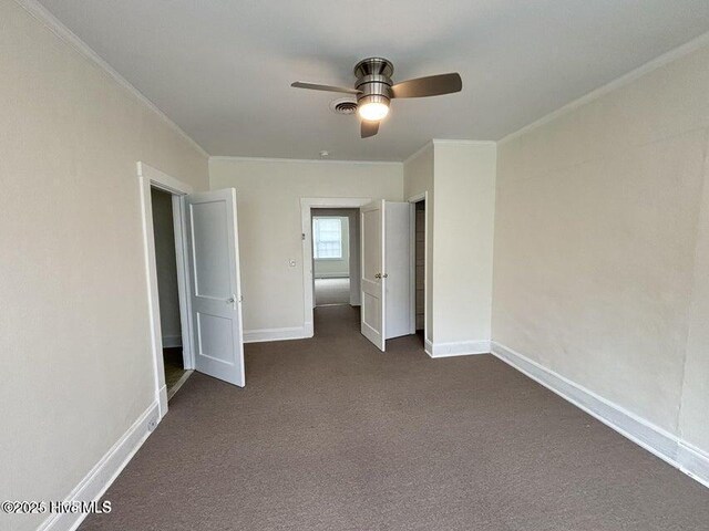 unfurnished bedroom featuring baseboards, visible vents, dark carpet, and crown molding