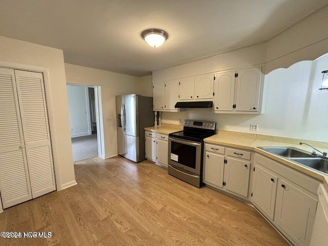 kitchen with light wood finished floors, a sink, under cabinet range hood, white cabinets, and appliances with stainless steel finishes