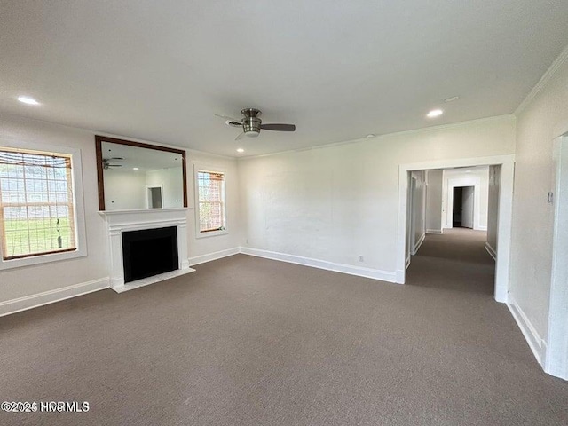 unfurnished living room featuring dark colored carpet, a ceiling fan, ornamental molding, and a fireplace with flush hearth