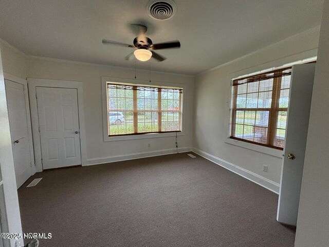 unfurnished room with dark carpet, a wealth of natural light, visible vents, and ceiling fan