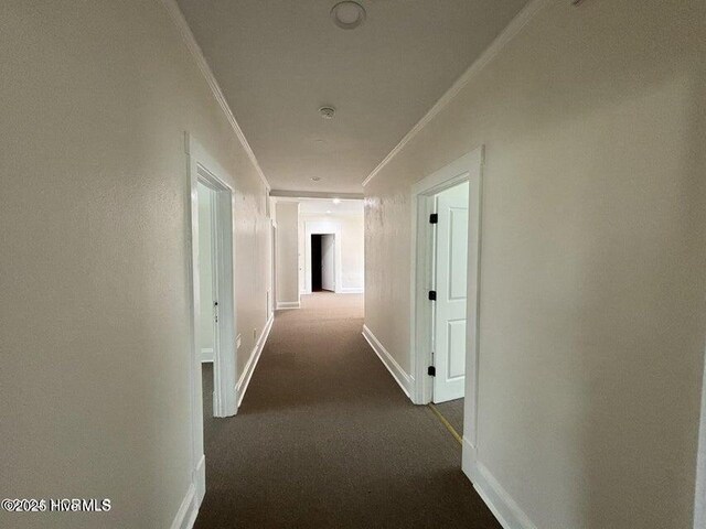 hall with baseboards, dark colored carpet, and crown molding