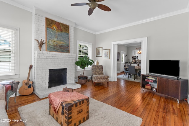 living room featuring wood-type flooring, ornamental molding, a fireplace, baseboards, and ceiling fan