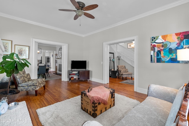 living room featuring a ceiling fan, baseboards, ornamental molding, stairs, and hardwood / wood-style floors