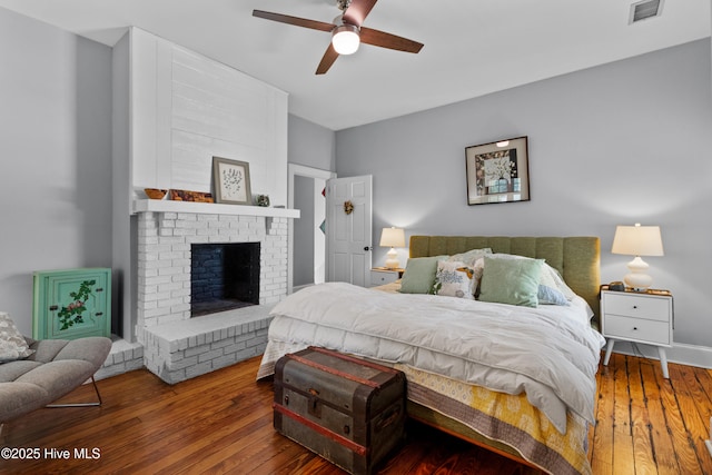 bedroom with a brick fireplace, ceiling fan, visible vents, and hardwood / wood-style flooring
