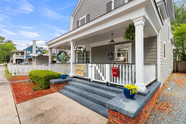 view of exterior entry with a porch and fence