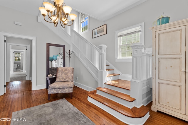 staircase featuring baseboards, hardwood / wood-style flooring, and a notable chandelier