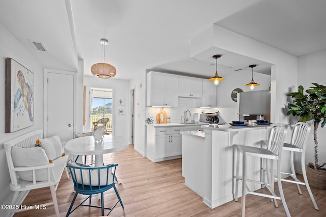 kitchen featuring a sink, tasteful backsplash, light wood finished floors, light countertops, and white cabinets