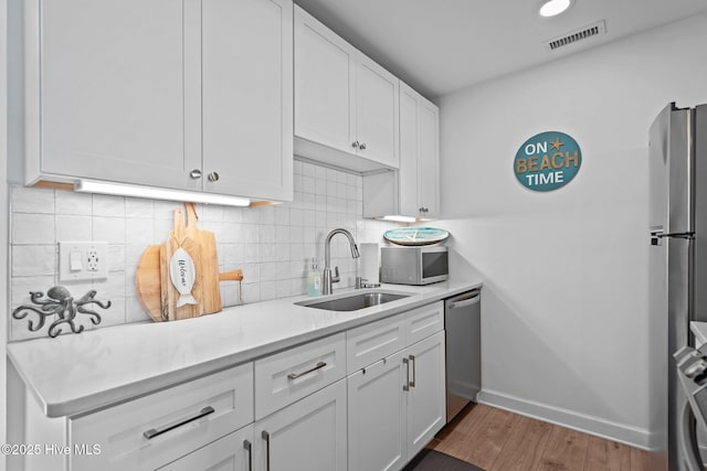 kitchen with a sink, stainless steel appliances, white cabinetry, visible vents, and light countertops