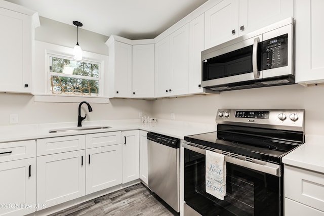 kitchen with a sink, stainless steel appliances, light wood finished floors, light countertops, and white cabinetry
