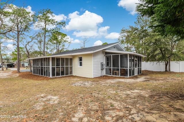 rear view of property with fence, a sunroom, and roof with shingles