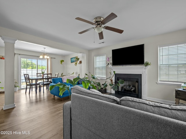 living area featuring a fireplace, ceiling fan with notable chandelier, baseboards, wood finished floors, and visible vents