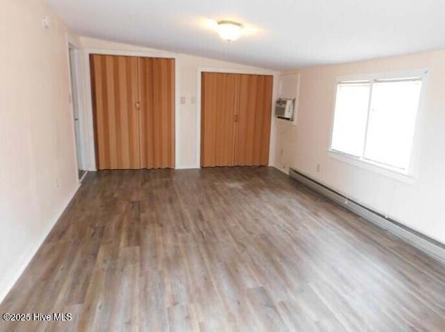 unfurnished bedroom with an AC wall unit, a baseboard radiator, wood finished floors, and lofted ceiling