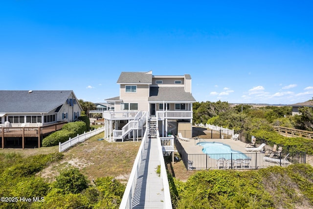 601 Caswell Beach Rd, Caswell Beach, NC 28465 - rear view of house with stairs, a fenced backyard, a patio area, a community pool, and roof with shingles