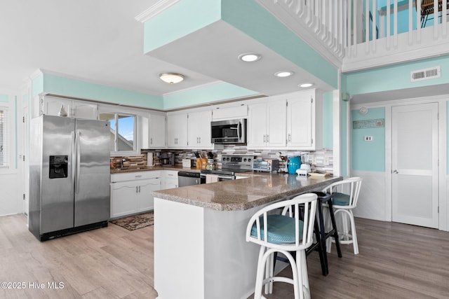 601 Caswell Beach Rd, Caswell Beach, NC 28465 - kitchen with stainless steel appliances, light wood finished floors, white cabinets, a peninsula, and visible vents