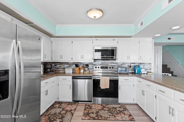 601 Caswell Beach Rd, Caswell Beach, NC 28465 - kitchen with white cabinets, stainless steel appliances, tasteful backsplash, light wood-type flooring, and ornamental molding