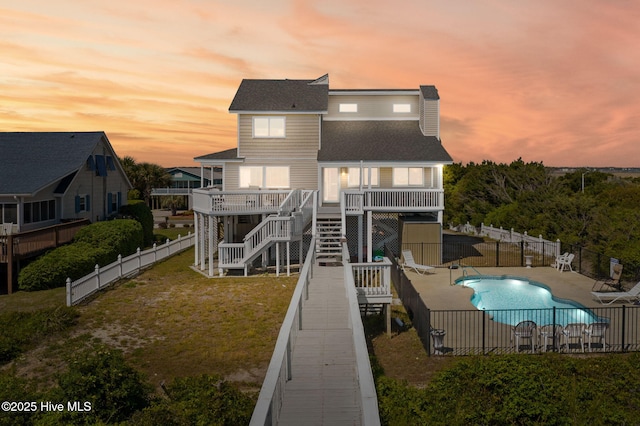 601 Caswell Beach Rd, Caswell Beach, NC 28465 - back of house at dusk with stairway, a fenced in pool, a fenced backyard, a lawn, and a deck