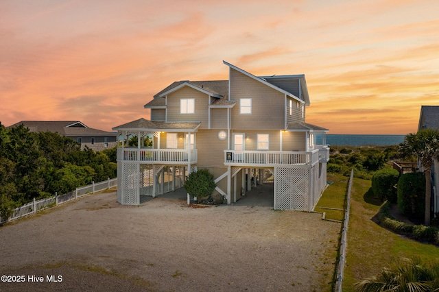 601 Caswell Beach Rd, Caswell Beach, NC 28465 - back of house at dusk with dirt driveway, stairway, a carport, and fence