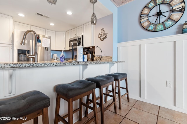 kitchen with light stone countertops, light tile patterned floors, visible vents, white cabinetry, and appliances with stainless steel finishes