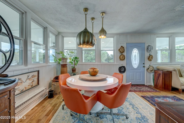 dining area with a baseboard heating unit, a textured ceiling, and light wood-style floors