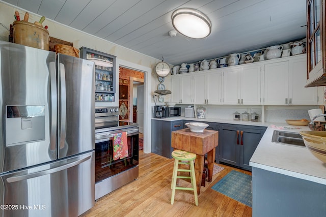 kitchen with white cabinets, a sink, light wood-style floors, light countertops, and appliances with stainless steel finishes