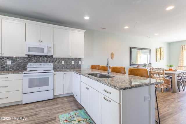 kitchen with light wood-type flooring, a sink, a peninsula, and white appliances