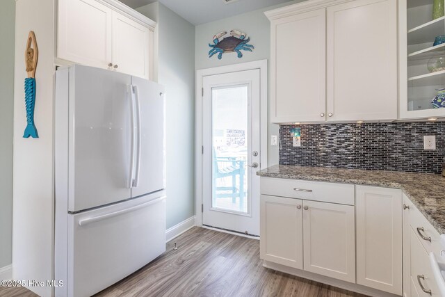 kitchen with light wood-type flooring, stone countertops, freestanding refrigerator, glass insert cabinets, and white cabinetry