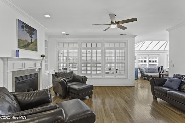 living area with a glass covered fireplace, recessed lighting, wood finished floors, ceiling fan, and crown molding