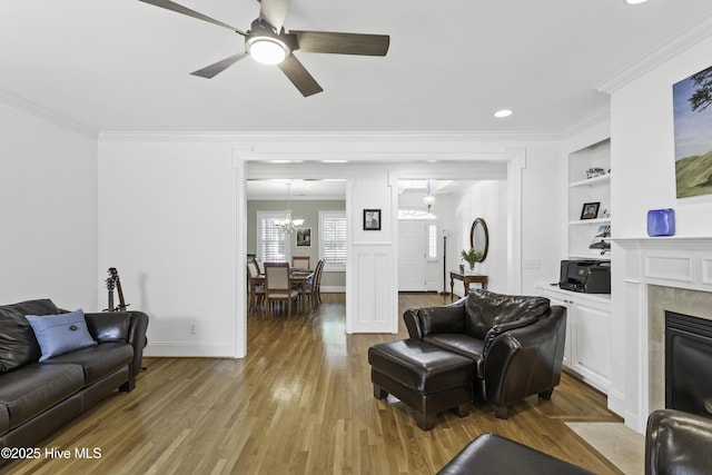 living room featuring light wood finished floors, built in shelves, ornamental molding, and ceiling fan with notable chandelier