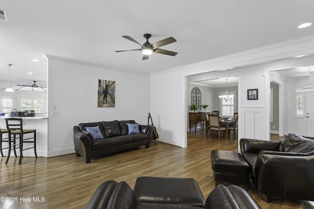 living room featuring wood finished floors, visible vents, crown molding, baseboards, and ceiling fan with notable chandelier