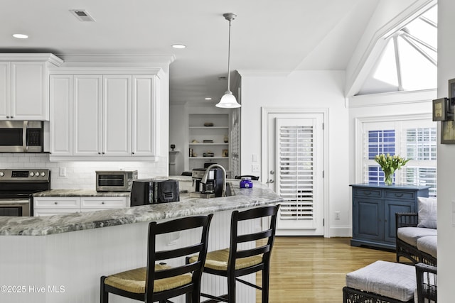 kitchen featuring decorative backsplash, a breakfast bar, stainless steel appliances, white cabinetry, and light stone countertops