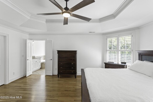 bedroom with a tray ceiling, ornamental molding, dark wood-type flooring, ensuite bath, and ceiling fan