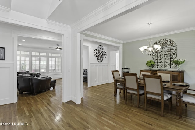 dining space featuring a decorative wall, ornamental molding, wood finished floors, and ceiling fan with notable chandelier