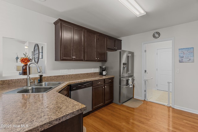 kitchen featuring a sink, appliances with stainless steel finishes, dark brown cabinets, light wood-style floors, and baseboards
