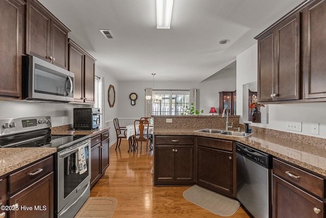kitchen featuring appliances with stainless steel finishes, a sink, light wood-type flooring, a peninsula, and dark brown cabinetry