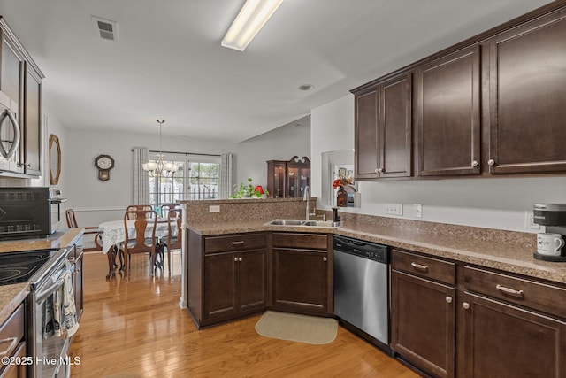 kitchen with stainless steel appliances, a sink, a peninsula, a chandelier, and light wood-style floors