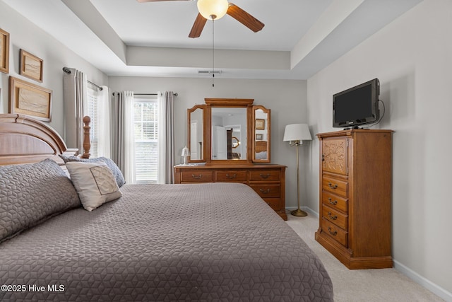 bedroom featuring baseboards, light carpet, a raised ceiling, and ceiling fan