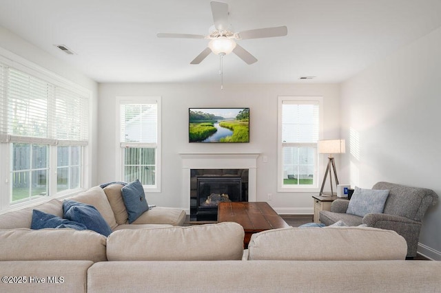 living room with a premium fireplace, a ceiling fan, visible vents, and baseboards