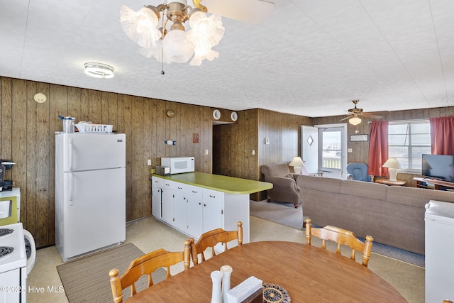 dining area with ceiling fan with notable chandelier and wooden walls