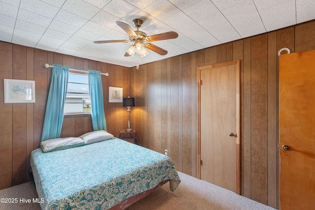 bedroom featuring ceiling fan, wooden walls, and carpet flooring