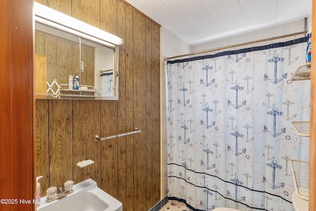 full bath featuring a shower with curtain, wooden walls, and a sink